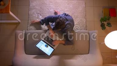 一位年轻商人的特写镜头，他在室内坐在地板上，在笔记本电脑上制作一张图表